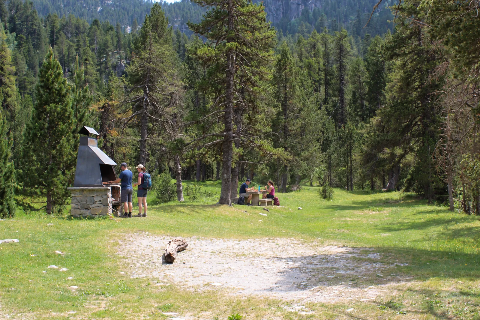 Excursionistas en la mesa y dos personas junto al asador de la zona de picnic de Era Montanheta